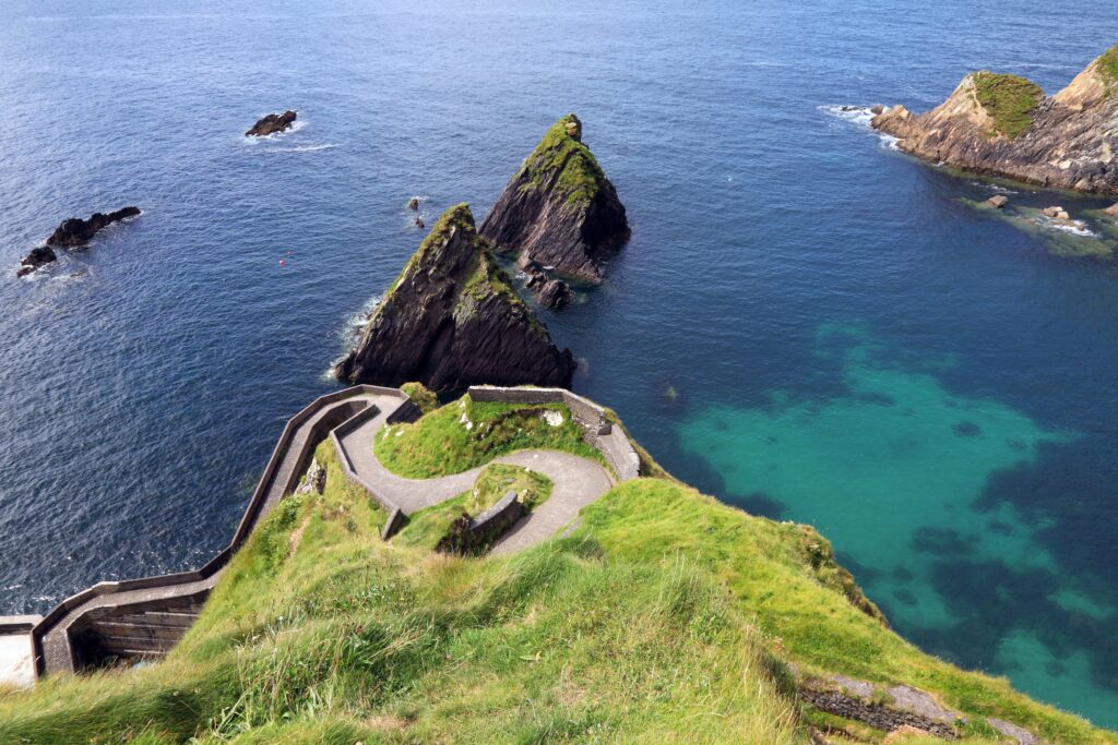 Winding coastal road on green clifftop overlooking turquoise sea and dark rock formations