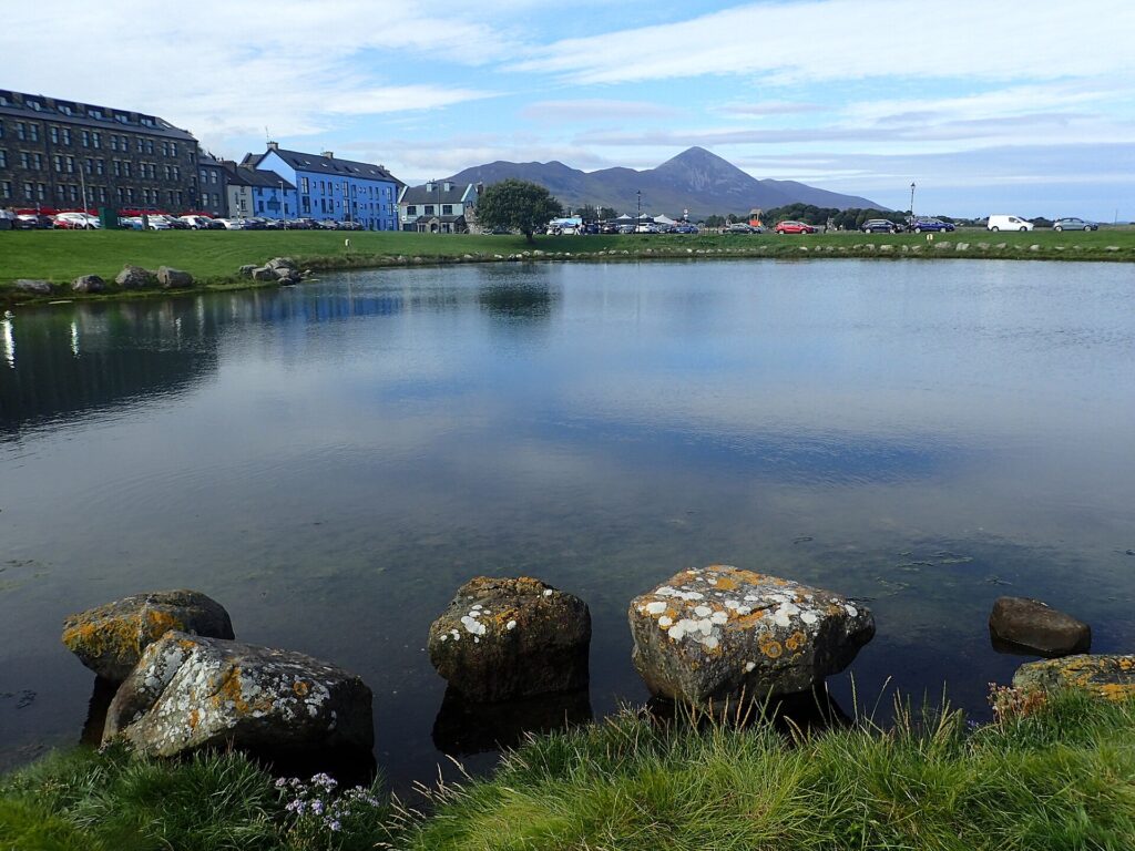 Lichen-covered rocks in shallow water with Irish coastal village and mountains beyond