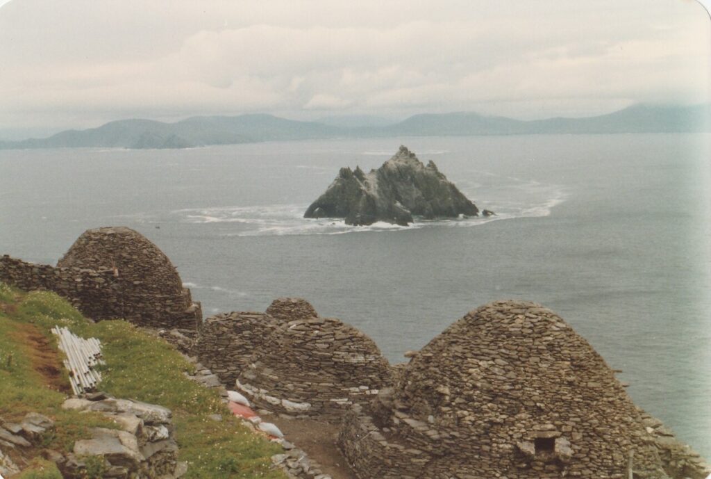 Stone beehive huts on grassy coastal cliff overlooking rocky island in sea