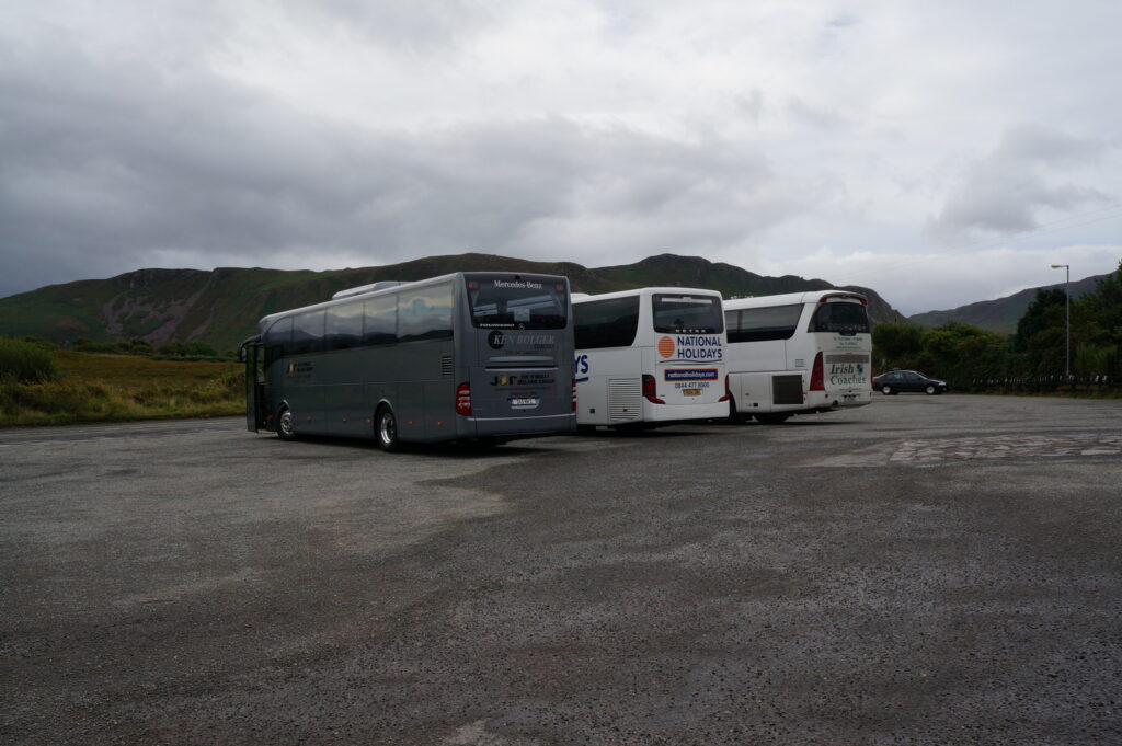 Three tour buses parked in a valley with green hills under cloudy sky