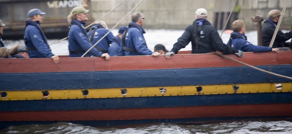 Group of people in blue jackets aboard a traditional wooden boat on water