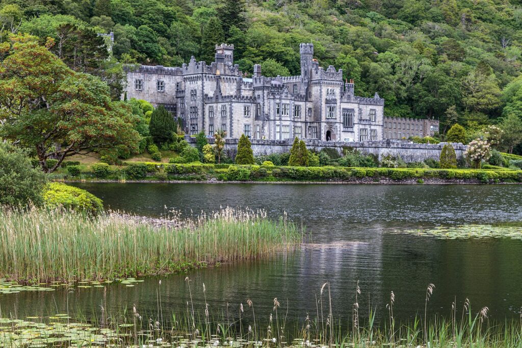 Gothic castle with towers reflected in calm lake, surrounded by lush green woodland