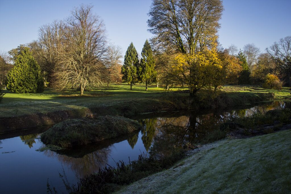 Tranquil river winding through autumn parkland with bare and evergreen trees