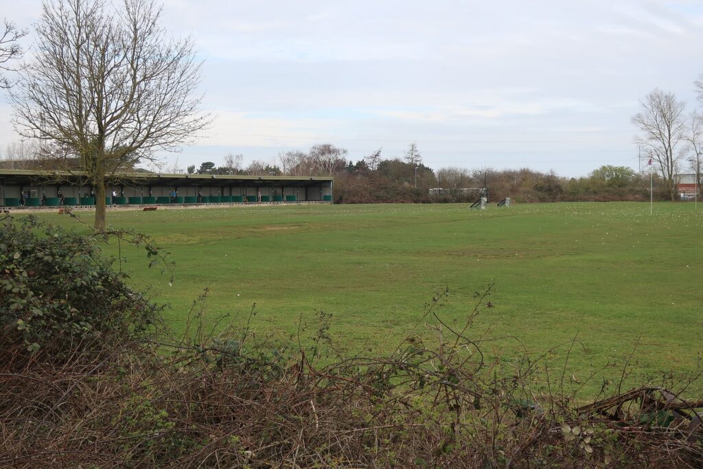 Grass sports field with green pavilion building and bare winter trees