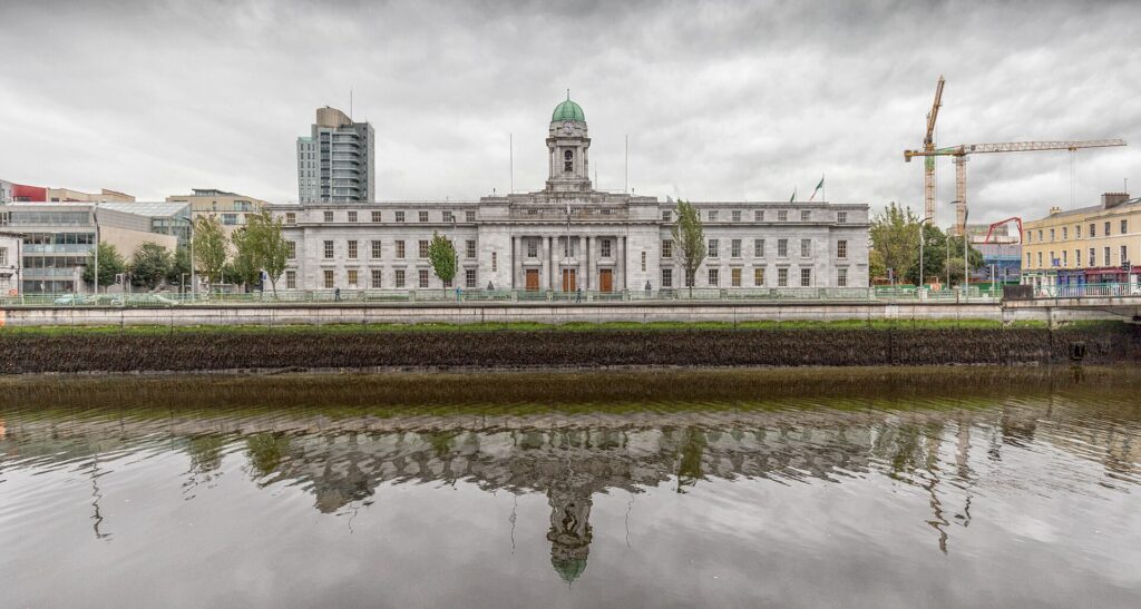 White neoclassical building with green dome reflected in calm river water