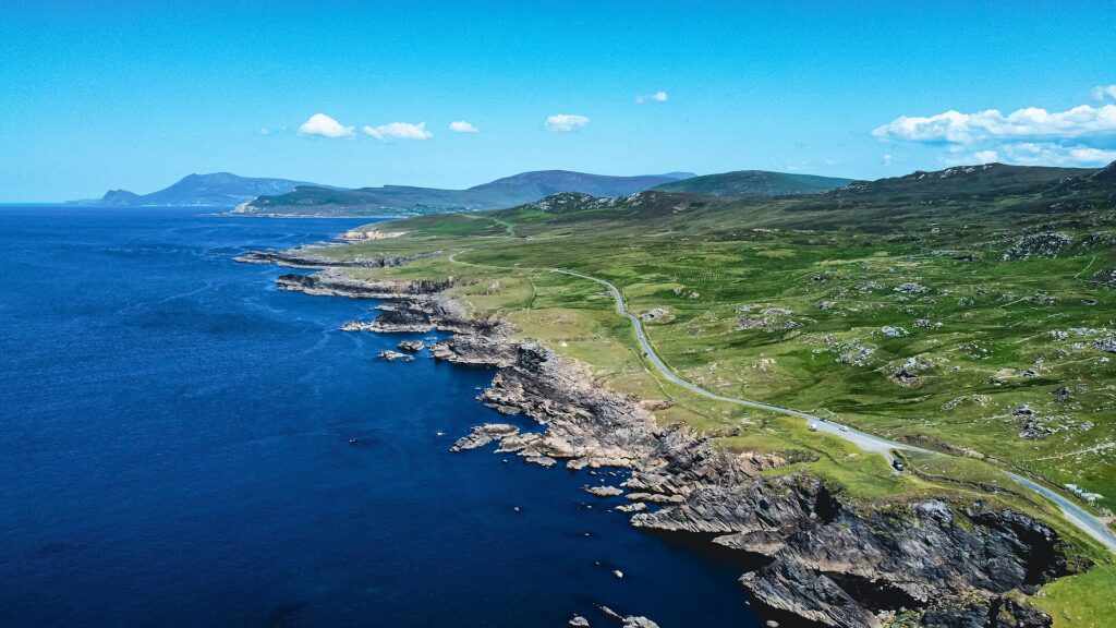 Aerial view of dramatic rocky coastline with green fields and winding road
