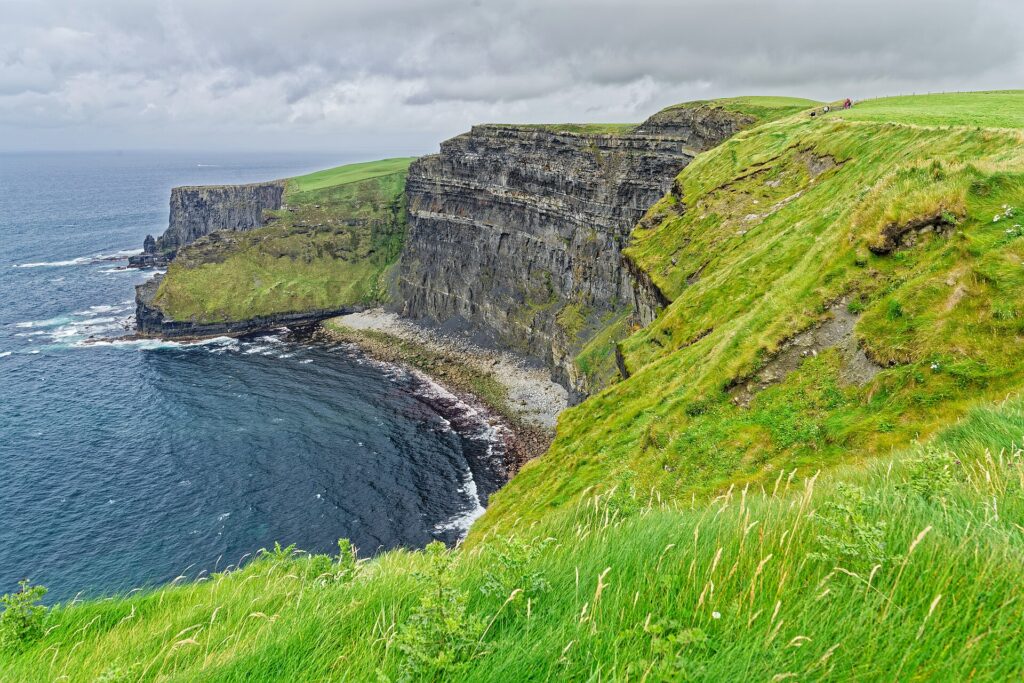 Steep green hillside overlooking dark ocean waters and dramatic basalt sea cliffs