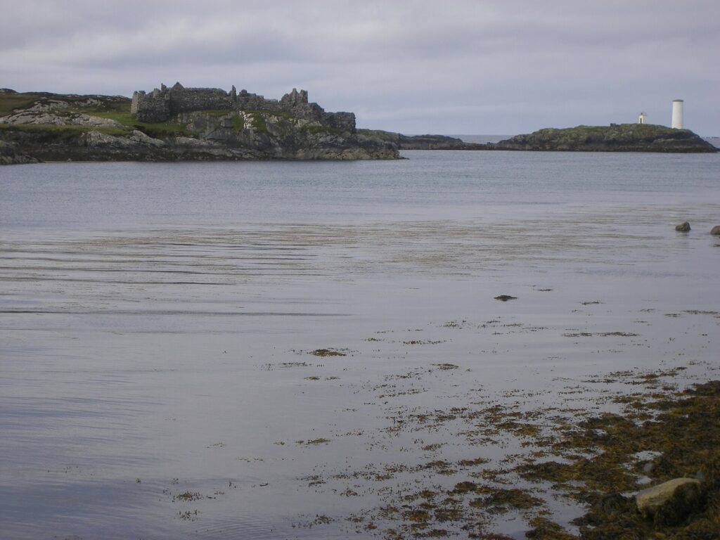 Ruined castle on rocky island with lighthouse across bay at low tide