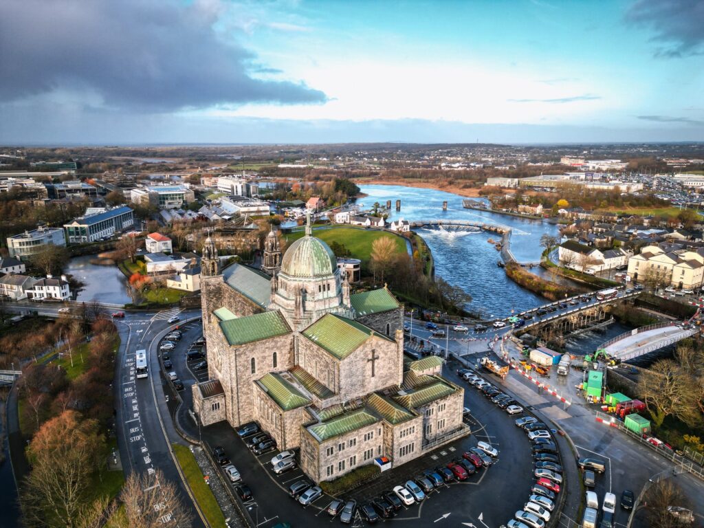 Aerial view of stone cathedral with green copper dome beside blue river and town
