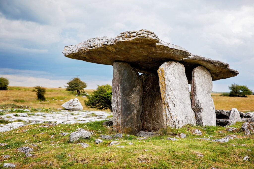 Ancient dolmen with flat capstone supported by three upright stones in grassy field