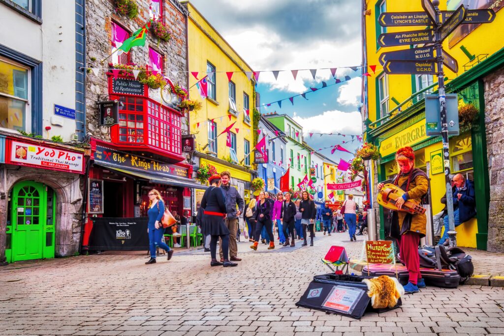 Colorful street scene with musicians, shops, and bunting in Irish town square