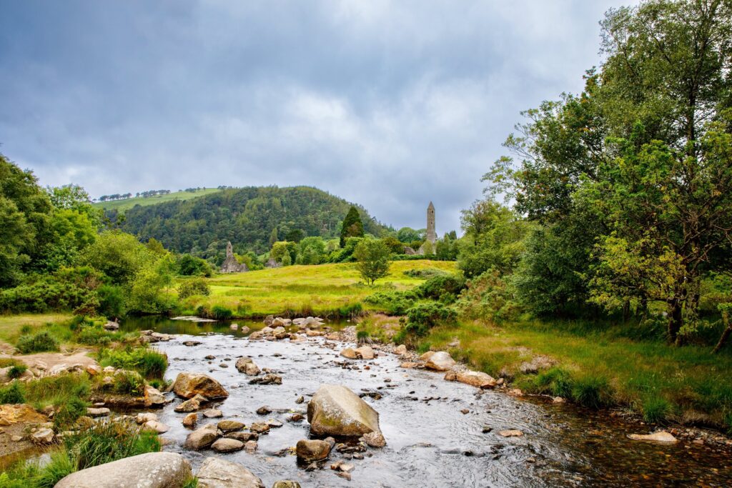 Rocky stream flows through lush green valley with round tower and ruins visible on distant hillside
