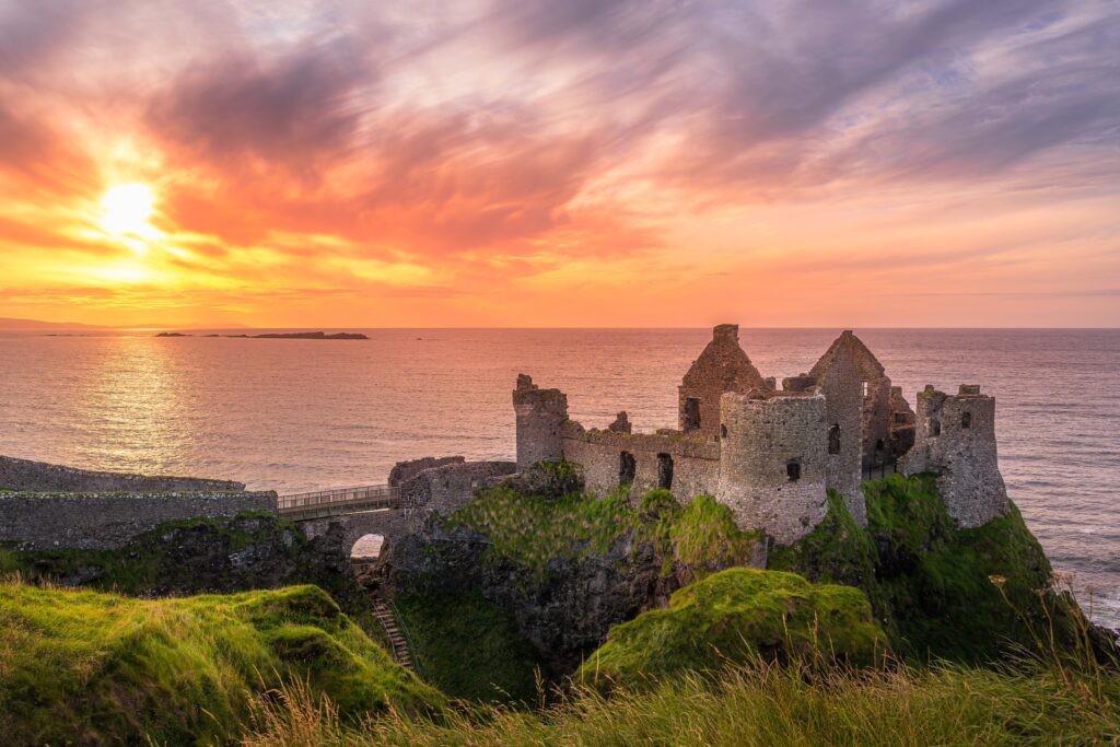 Medieval stone castle ruins on coastal cliff at sunset with golden sky