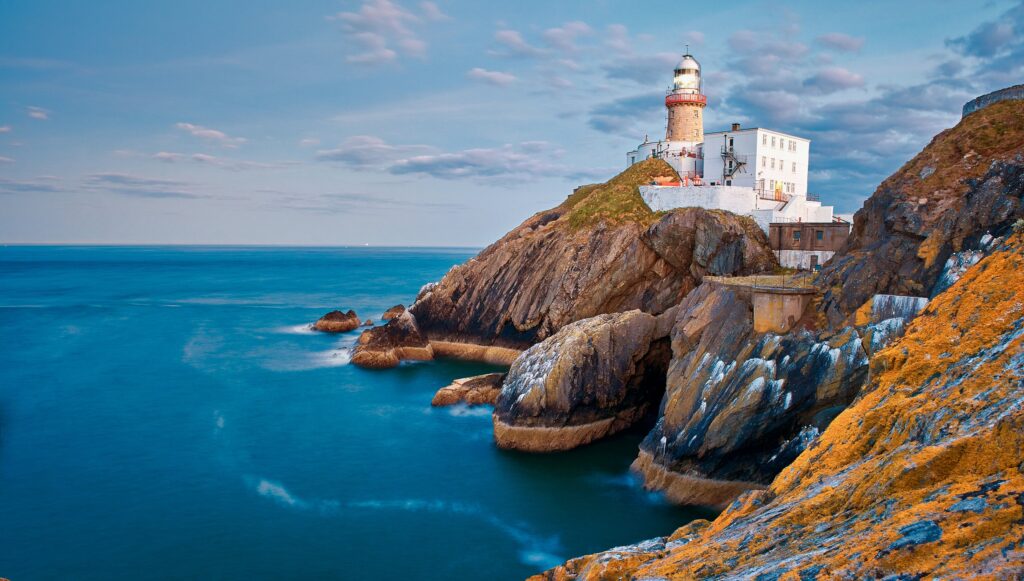 White lighthouse with red top on rocky coastal cliff overlooking turquoise sea