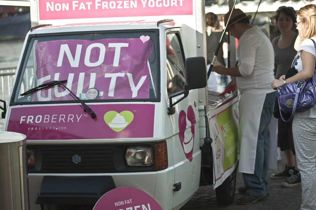 Purple and white frozen yogurt food truck with queue of customers