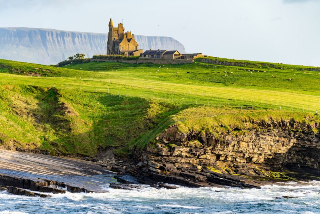 Yellow stone church with tower on green clifftop overlooking rocky coastline and ocean