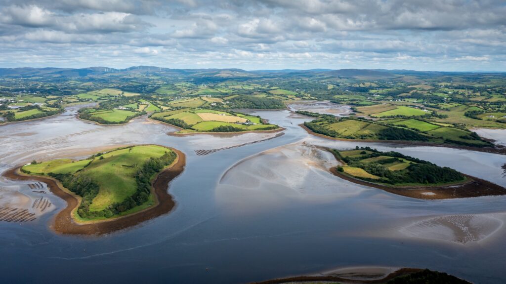 Aerial view of winding river with tidal mudflats and green islands surrounded by farmland