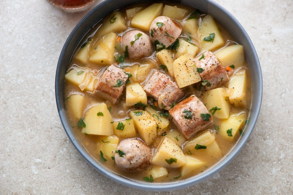 Bowl of Irish stew with sausages, potatoes, and fresh parsley garnish
