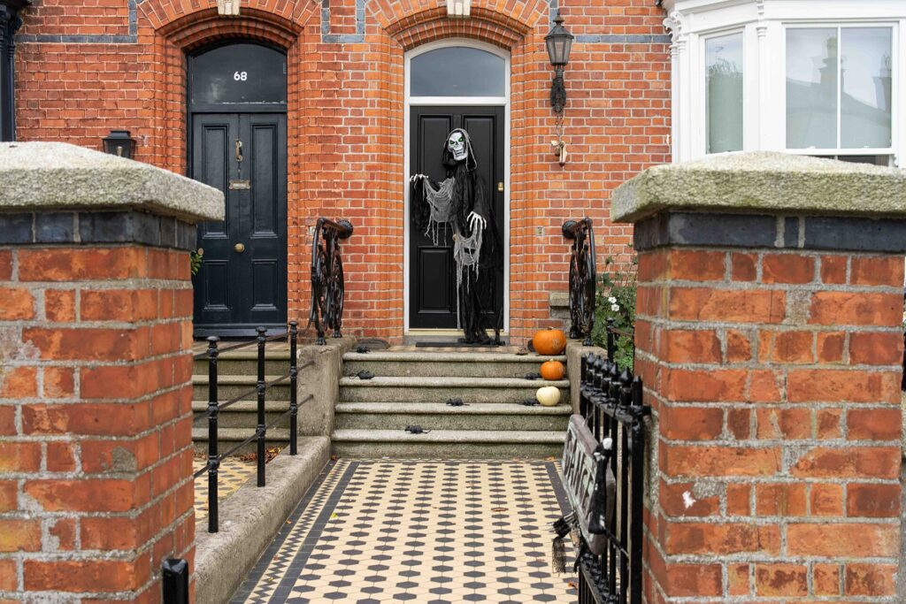 Halloween-decorated Victorian townhouse entrance with skeleton artwork and pumpkins