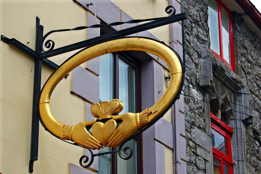 Golden Claddagh ring sign with black wrought iron bracket on colorful building facade