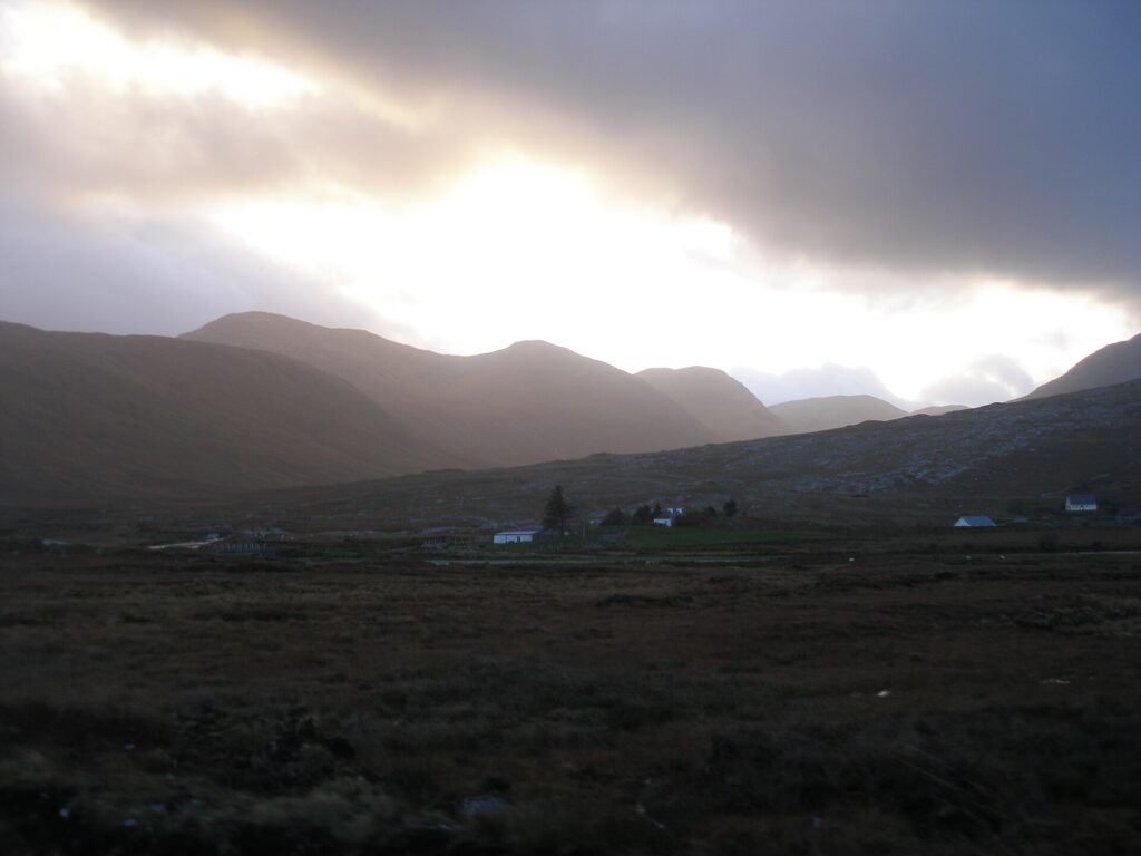 Rural valley with scattered houses beneath dramatic mountains and cloudy sky