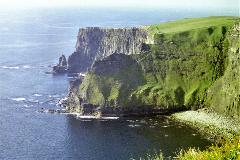 Dramatic green sea cliffs with distinctive columnar basalt formations and grassy plateau overlooking Atlantic Ocean