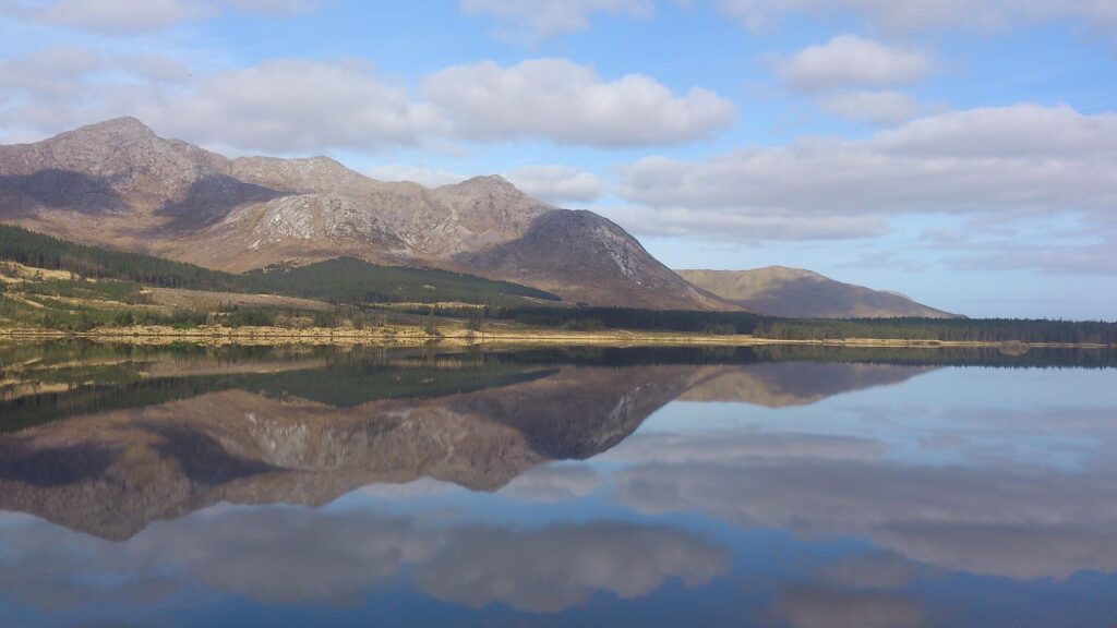 Mountain range reflected in still lake water under cloudy sky