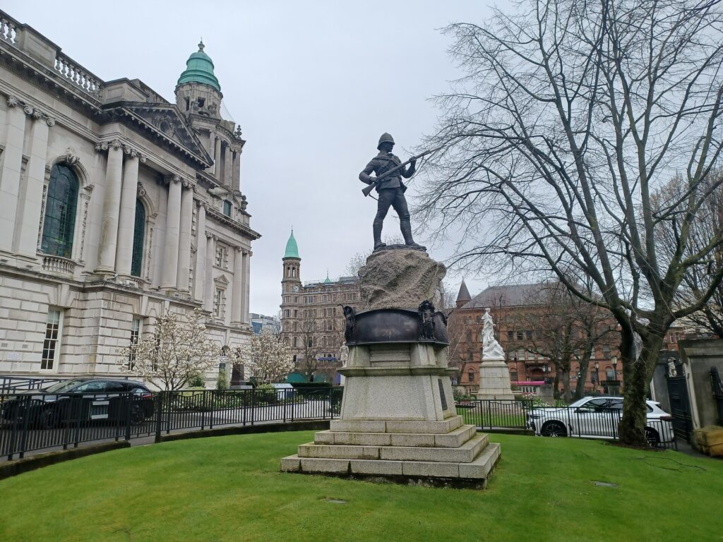Statue of armed soldier on stone pedestal in city square with neoclassical building