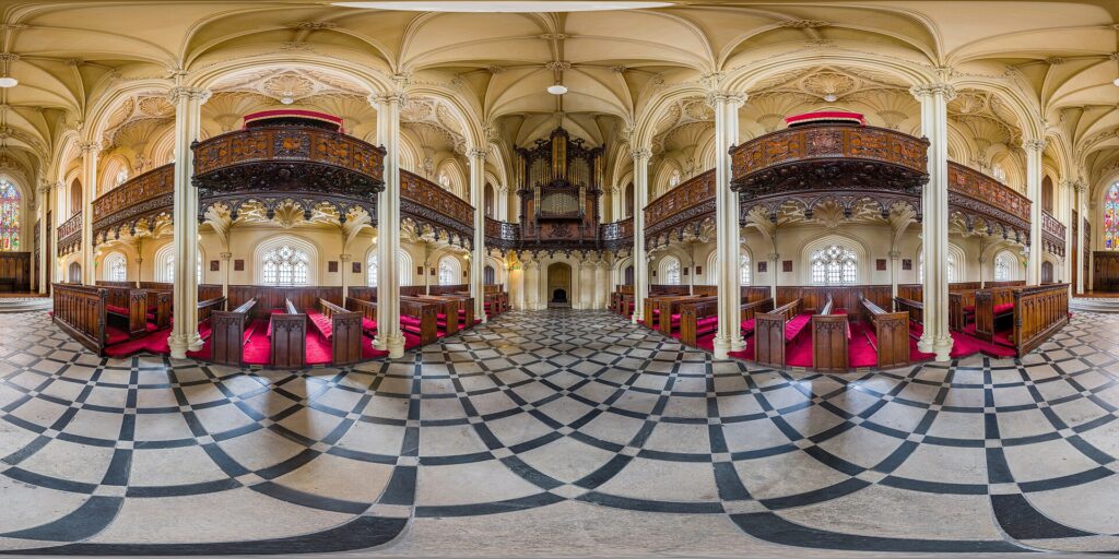 Interior of ornate church with wooden pews, organ, and geometric floor pattern