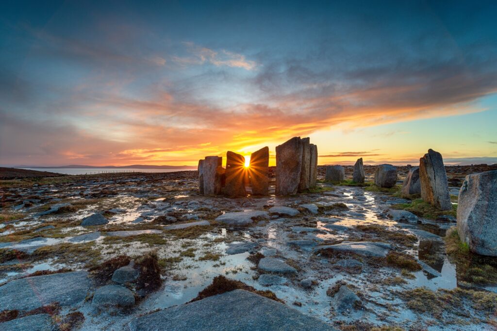 Ancient standing stones silhouetted against golden sunset sky