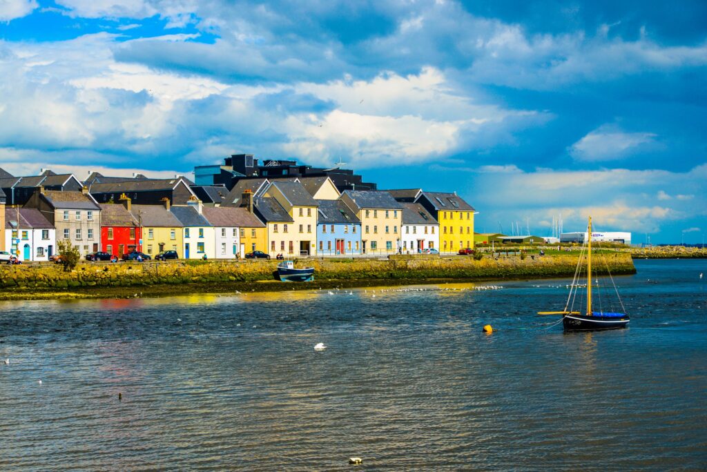 Colorful waterfront houses reflected in calm harbor water with sailboat