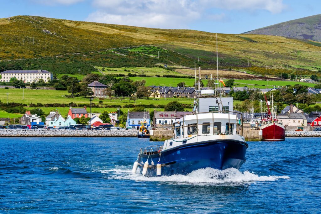 Blue and white fishing boat departing from Irish coastal harbor village