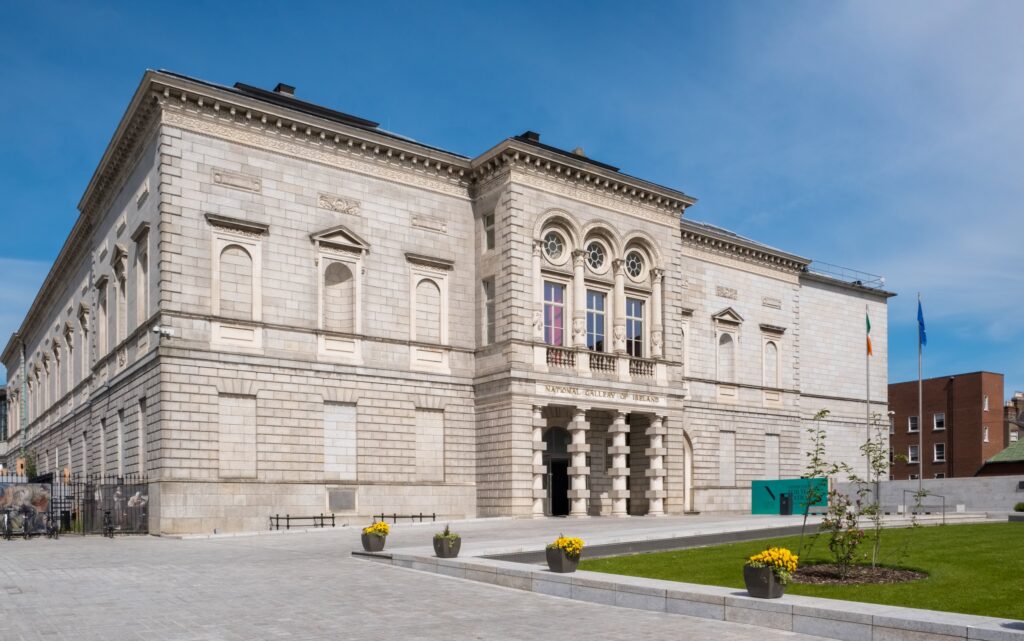 Neo-classical stone building with ornate entrance and manicured grounds under blue sky