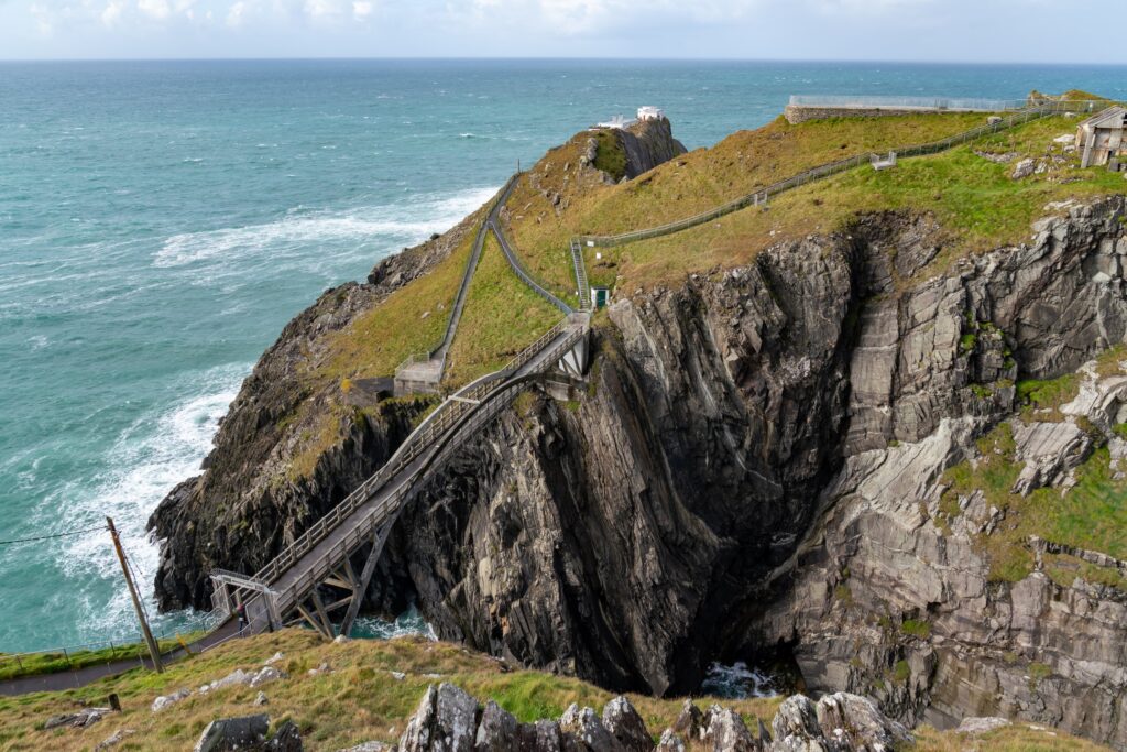 Wooden bridge crossing rocky chasm on grassy Irish coastal headland