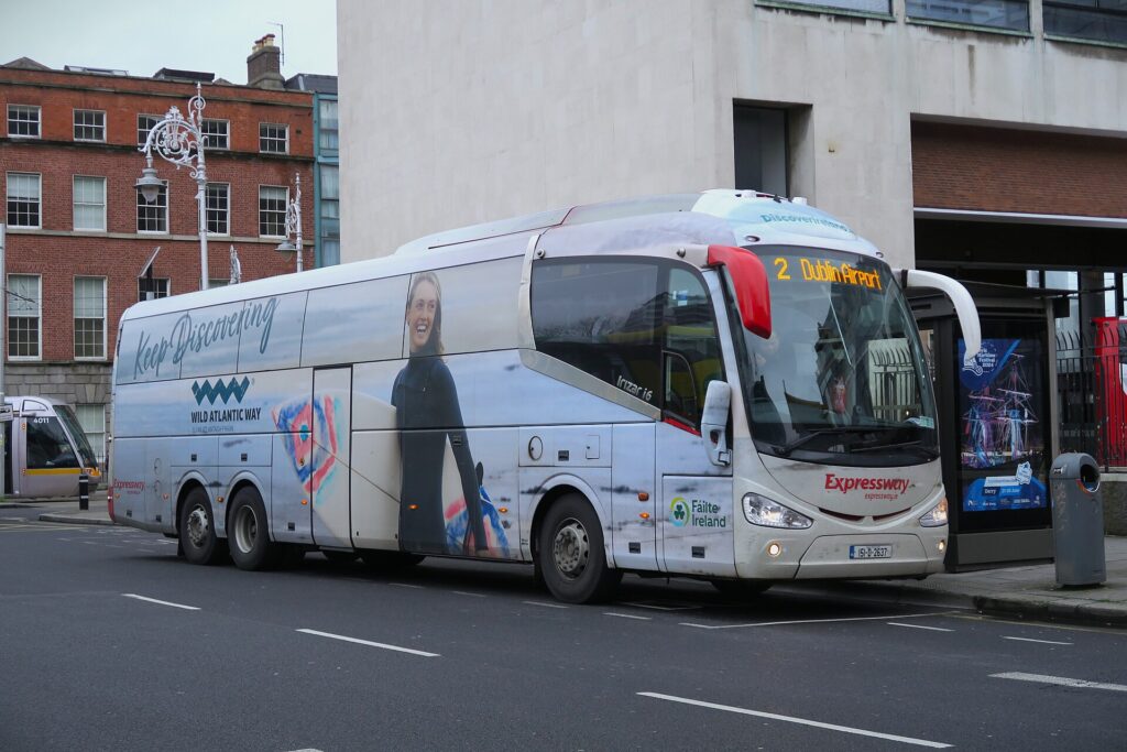 White double-decker coach bus parked on Irish street with historic brick building