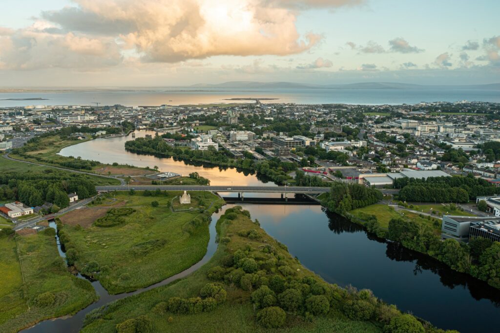 Aerial view of Irish river valley with bridge, green fields, and coastal town beyond