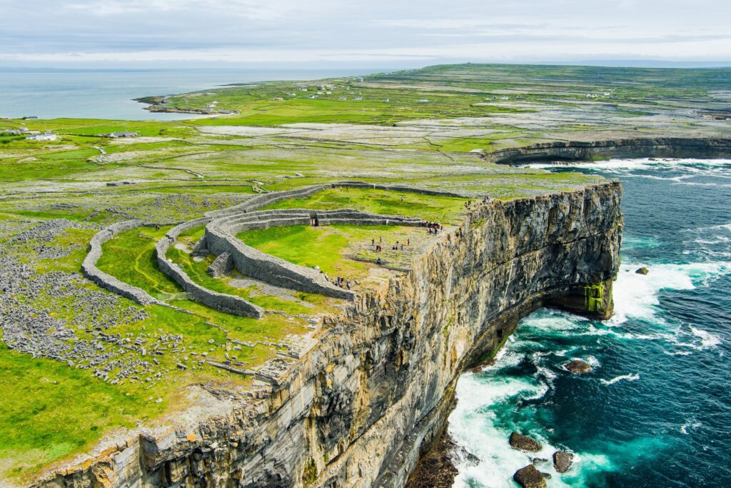 Aerial view of dramatic coastal cliffs with curved stone walls and lush green fields