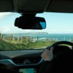 A man driving a car down a road next to the ocean